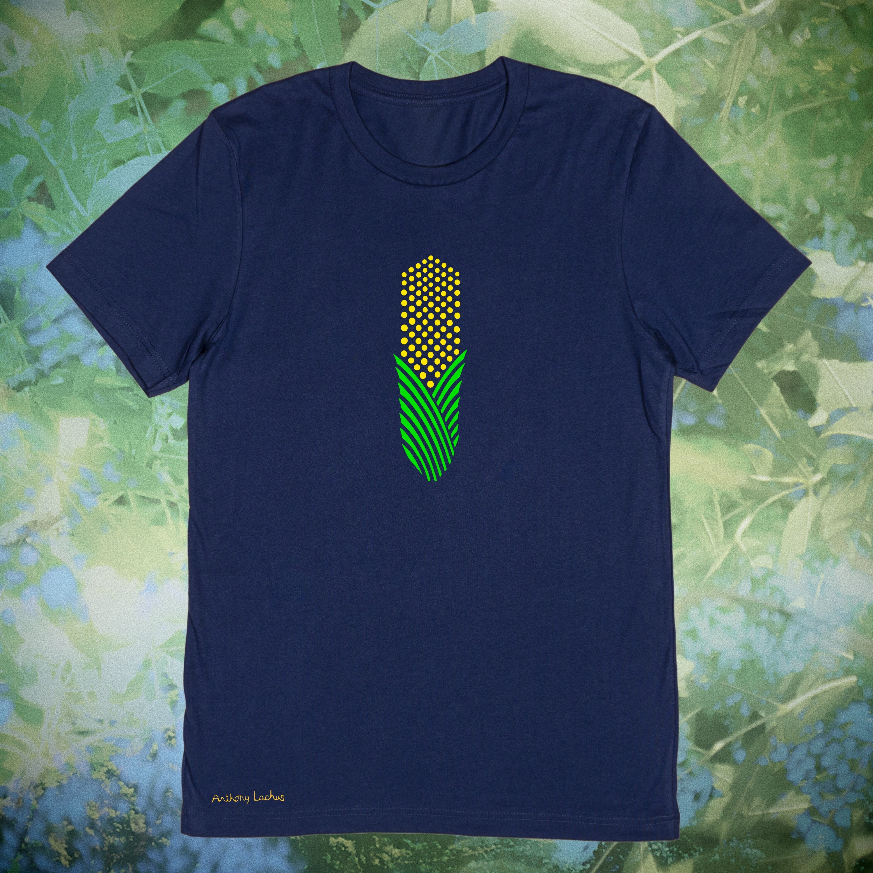 A navy blue short-sleeve t-shirt with a central graphic of a green and yellow corn cob, displayed against a blurred green foliage background.