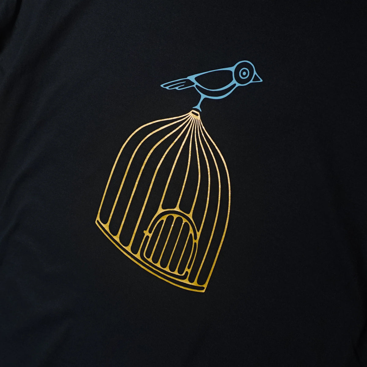 A close-up of a black t-shirt featuring a graphic print of a gold birdcage with a light blue bird perched on top.