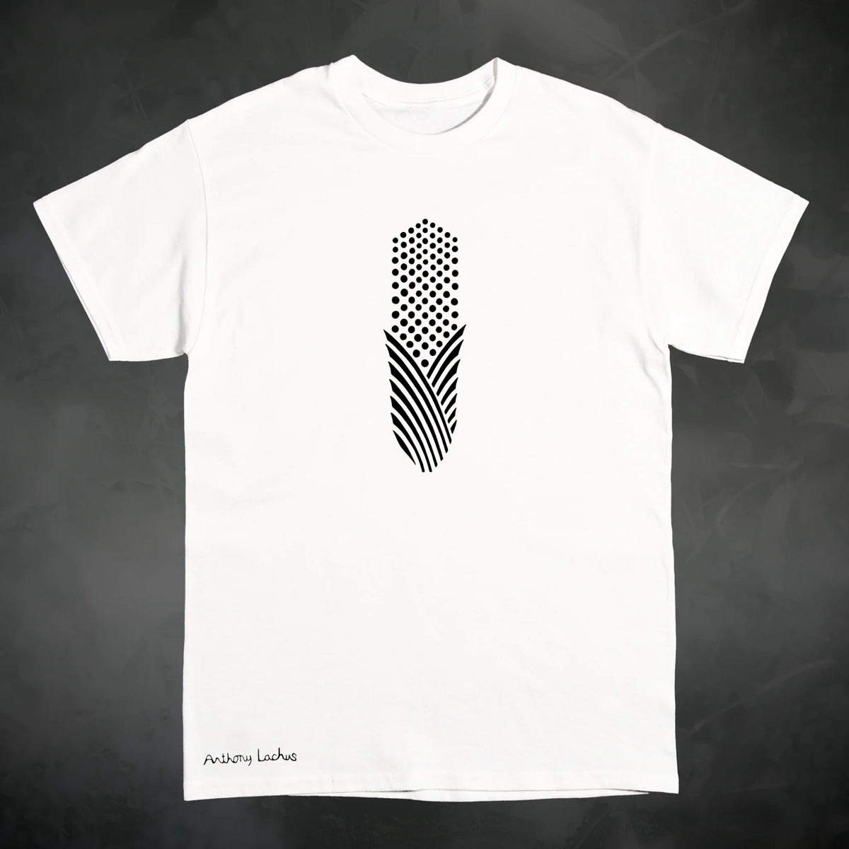 A white short sleeve Gildan g500 crewneck t-shirt featuring a graphic design of a black piece of corn, laid flat on a textured dark gray background. Original hand drawn artwork by Anthony Lachus. Signature on lower left of the shirt. Front view.